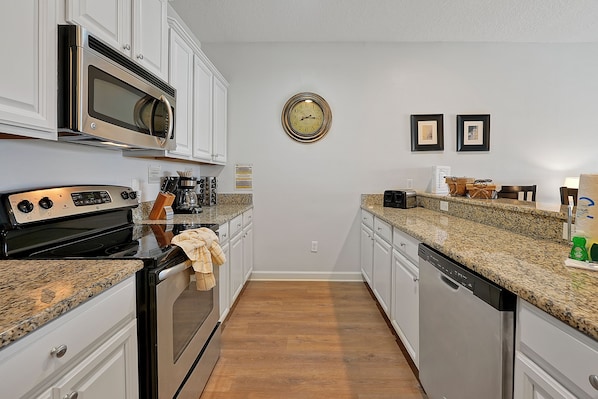 A kitchen with white cabinets, a stainless steel microwave, a stove, and a dishwasher. - Private Pool, Waterview, No Rear Neighbors | Paradise Palms Resort (Kissimmee)