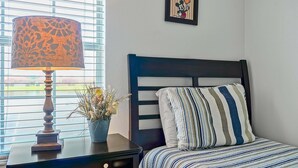 A bedroom with a bed, a nightstand with a lamp, a potted plant, and a Mickey Mouse framed picture on the wall. - Private Pool, Waterview, No Rear Neighbors | Paradise Palms Resort (Kissimmee)