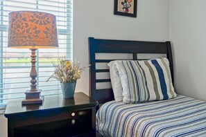 A bedroom with a bed, a nightstand with a lamp, a potted plant, and a Mickey Mouse framed picture on the wall. - Private Pool, Waterview, No Rear Neighbors | Paradise Palms Resort (Kissimmee)