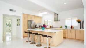 A modern kitchen with a central island, bar stools, and a large window.