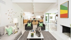 A modern living room with a sofa, coffee table, and patterned rug. There is a kitchen in the background with a dining area visible.