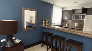 Een kleine hotelkamer met kitchenette, spiegel, lamp en drie barkrukken.