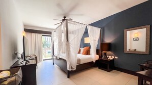 Een slaapkamer met een hemelbed, een plafondventilator, een nachtkastje met een lamp en een grote spiegel aan de muur.