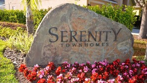 Un letrero de piedra con el texto "Serenity Townhomes" rodeado de flores de colores.