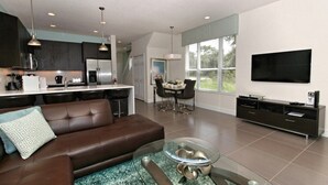Una sala de estar moderna con un sofá de cuero marrón, una mesa de centro de vidrio y una zona de comedor con mesa y sillas.