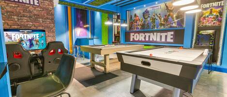 Una sala con dos mesas de billar, una zona de juegos temática de 'Fortnite' y una pared de ladrillo.