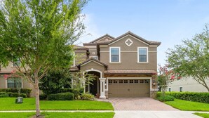 A two-story house with a garage, a front porch, and a well-maintained lawn. - Championsgate Resort 9 Bedroom Private Pool+Spa Home (Davenport)