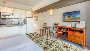 Ett hotellrum med en säng, ett skrivbord med en stol, en liten köksdel och en tavla på väggen.