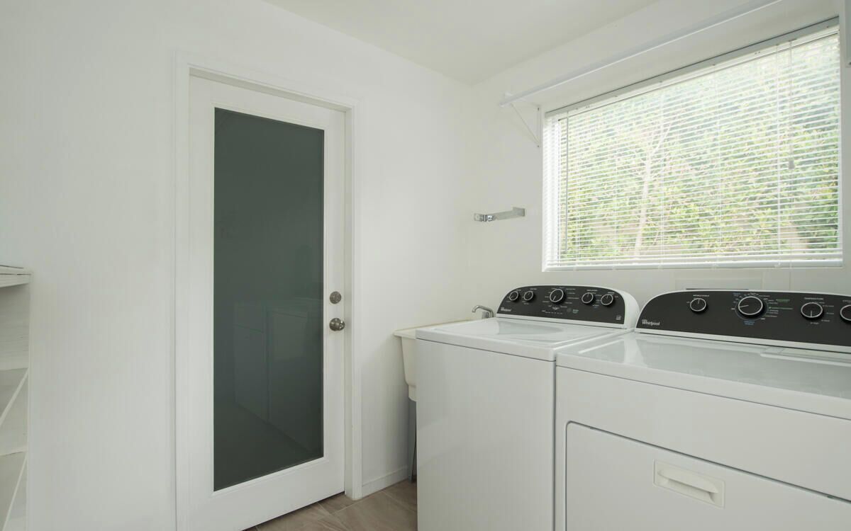 Un cuarto de lavandería con lavadora y secadora de carga frontal, una puerta con panel de vidrio esmerilado y una ventana con persianas.