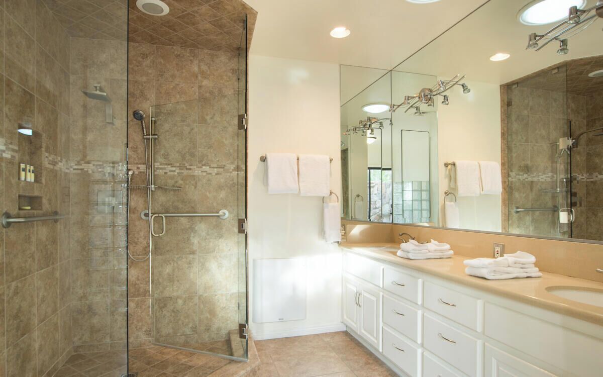 Une salle de bain moderne avec une douche à parois de verre, des meubles blancs et un grand miroir.