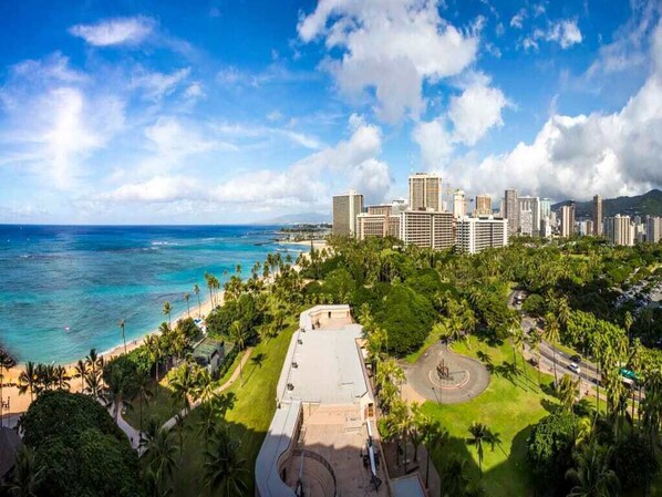 A coastal cityscape with a prominent hotel complex, a beach, and lush greenery.