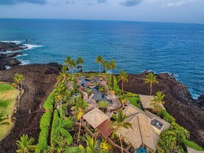 Vista aérea de un resort con una piscina central, rodeado de vegetación tropical y un litoral rocoso.