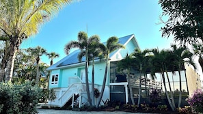 Una casa de dos pisos con fachada azul claro, un porche cubierto y paneles solares en el techo.