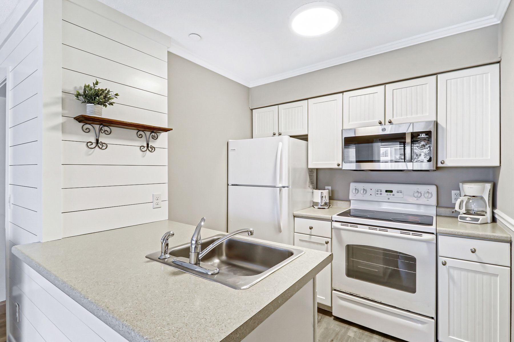 Une cuisine moderne avec des meubles blancs, un évier en acier inoxydable, un four encastré, un four à micro-ondes et une machine à café.