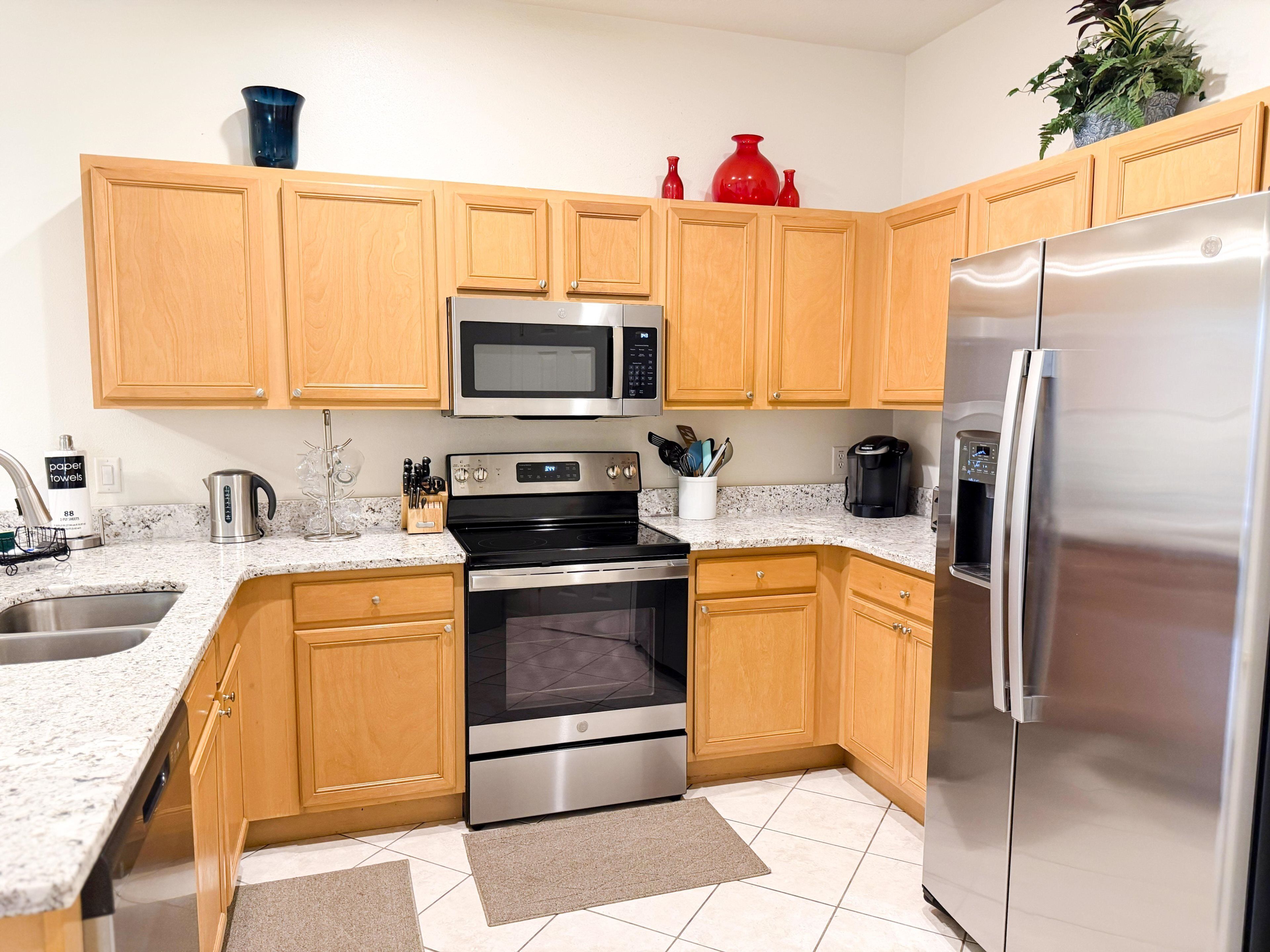 A modern kitchen with wooden cabinets, stainless steel appliances, granite countertops, and a tiled floor.