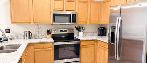 A modern kitchen with wooden cabinets, stainless steel appliances, granite countertops, and a tiled floor.
