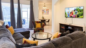 Ein Wohnzimmer mit einer Sofagarnitur, einem Glastisch, einem Fernseher und einem Deckenventilator.