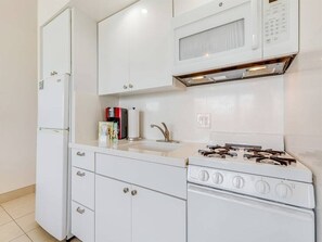A compact kitchen with white cabinetry, a microwave, a stove, and a refrigerator. - Beachy Penthouse w/Epic Ocean View, Free WiFi, Kitchenette–Waikīkī Shore PH03 (HONOLULU)