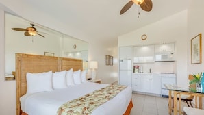 Ein Hotelzimmer mit einem großen Bett, einem Deckenventilator, einer Küchenzeile inklusive Mikrowelle und einem Esstisch.