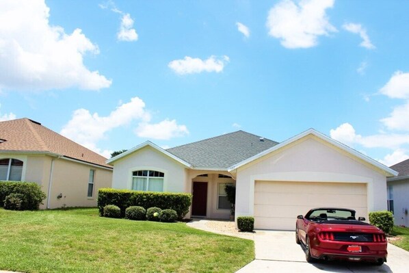 A single-story house with a garage, a driveway, and a red convertible parked in the garage. - Disney Area - 4 bedrooms / 2 bathrooms pool home with golf view (Davenport)