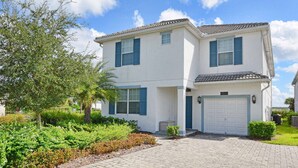 A two-story house with a white exterior and blue shutters, a garage, and a paved driveway.