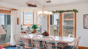 A dining area with a wooden table and chairs, a chandelier, and large windows with curtains.