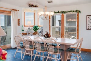 Un comedor con mesa y sillas de madera, una araña y ventanas grandes con cortinas.