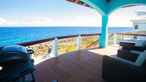 Un patio techado con vista al océano, mobiliario exterior y una parrilla.