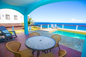 A patio with a pool, wicker furniture, and a view of the ocean. - Stunning Oceanfront Villa private pool, & Constant Sea Breeze (Roatan)