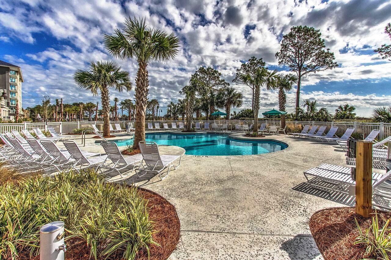 A pool area with lounge chairs, palm trees, and a building in the background.