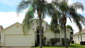 A single-story house with a white garage door, a front porch, and two palm trees.