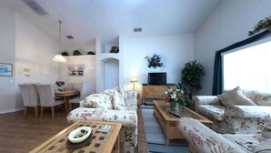 A modern living room with a sofa, coffee table, and a dining area with chairs and a table.
