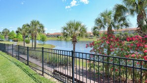 A waterfront park with a walking path, palm trees, and a body of water. - Waterfront Pool Townhome in Encantada Resort | Minutes to Disney (Kissimmee)