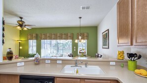 A kitchen with a dishwasher, a sink, wooden cabinets, a ceiling fan, and a window with blinds. - Waterfront Pool Townhome in Encantada Resort | Minutes to Disney (Kissimmee)
