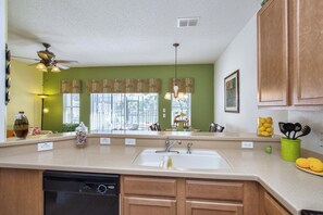 A kitchen with a dishwasher, a sink, wooden cabinets, a ceiling fan, and a window with blinds. - Waterfront Pool Townhome in Encantada Resort | Minutes to Disney (Kissimmee)