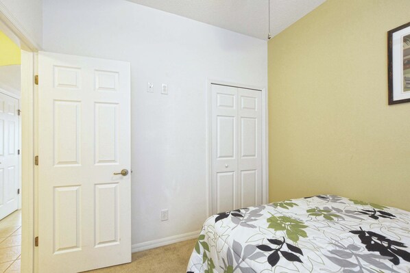 Une chambre à coucher avec un lit, deux portes blanches, un mur de couleur claire et un tableau encadré.