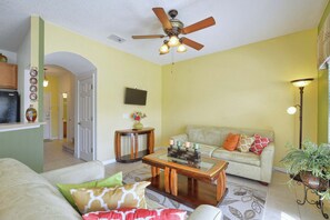 Un salon avec un ventilateur de plafond, un canapé, une table basse et un téléviseur.