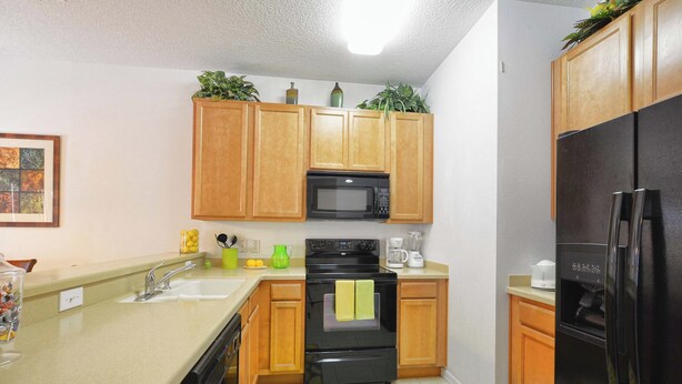 A kitchen with wooden cabinets, a black microwave, a stove, a refrigerator, and a sink. - Waterfront Pool Townhome in Encantada Resort | Minutes to Disney (Kissimmee)