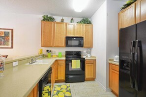 A kitchen with wooden cabinets, a black microwave, a stove, a refrigerator, and a sink. - Waterfront Pool Townhome in Encantada Resort | Minutes to Disney (Kissimmee)
