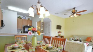A dining area with a wooden table set for a meal, a kitchen in the background, and a ceiling fan. - Waterfront Pool Townhome in Encantada Resort | Minutes to Disney (Kissimmee)
