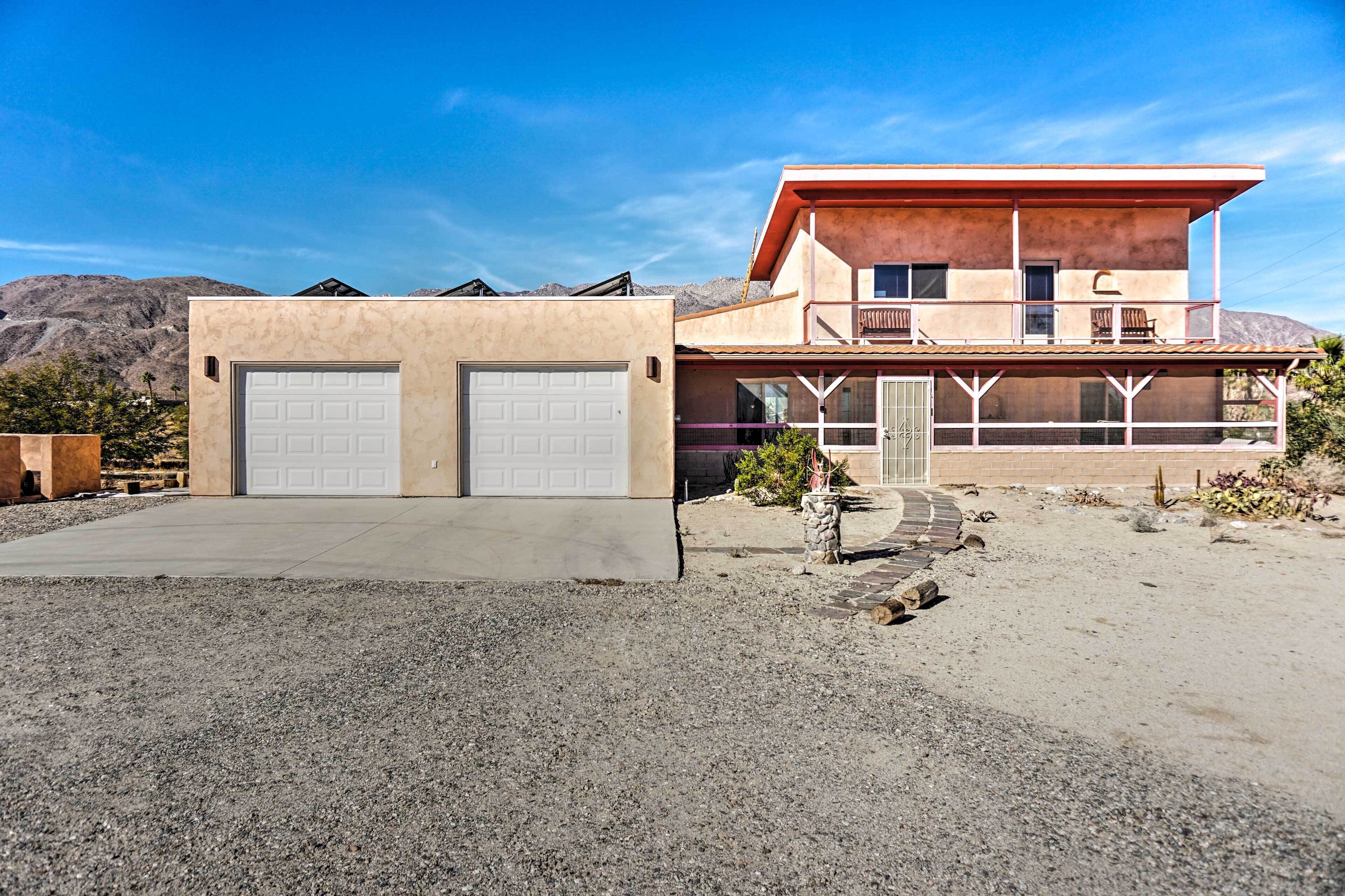 A two-story house with a garage, a balcony, and a desert landscape in the background.