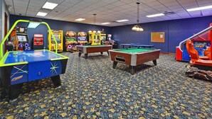 Una sala de recreación con mesas de billar, juegos de arcade y piso alfombrado.