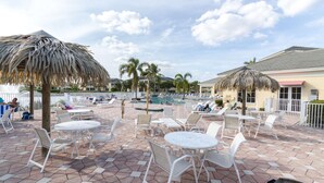 A poolside area with lounge chairs and tables, a pool, and palm trees.