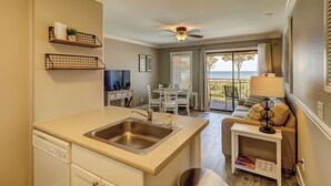 A compact kitchen with a sink, a dining area with a table and chairs, and a balcony with a view of the ocean. - Breathtaking Ocean Views with Year-Round Heated Pool! (Hilton Head Island)