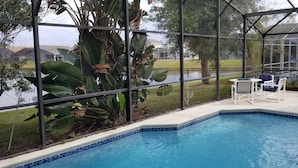 Ett poolområde med utsikt över en sjö, omgivet av stora, tropiska växter och en täckt sittplats med stolar.