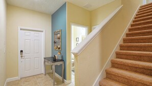 A hallway with a carpeted staircase, a white door, and a small table with a vase. - Paradise Palms | 2 King Beds | Private Splash Pool & BBQ | Dog Friendly (Kissimmee)