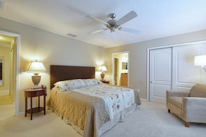 Une chambre à coucher avec un lit, deux tables de chevet avec des lampes, un ventilateur de plafond, une porte et une chaise.