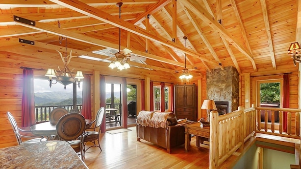 A wooden cabin interior with a dining area, a fireplace, and a balcony with a mountain view.