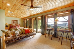 Una habitación acogedora con techo de madera, un sofá con muchos cojines, una mesa con sillas y vistas amplias a través de grandes ventanales.