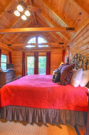 Un dormitorio de cabaña de madera con una cama grande, un aparador, un televisor y un balcón.